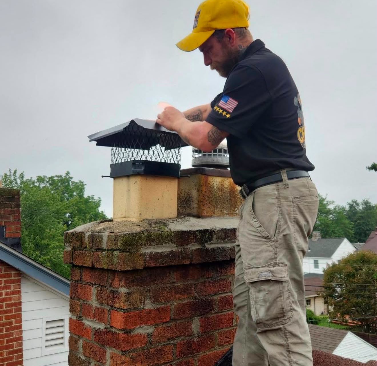 ChimCrew technician installing a black chimney cap on a brick chimney