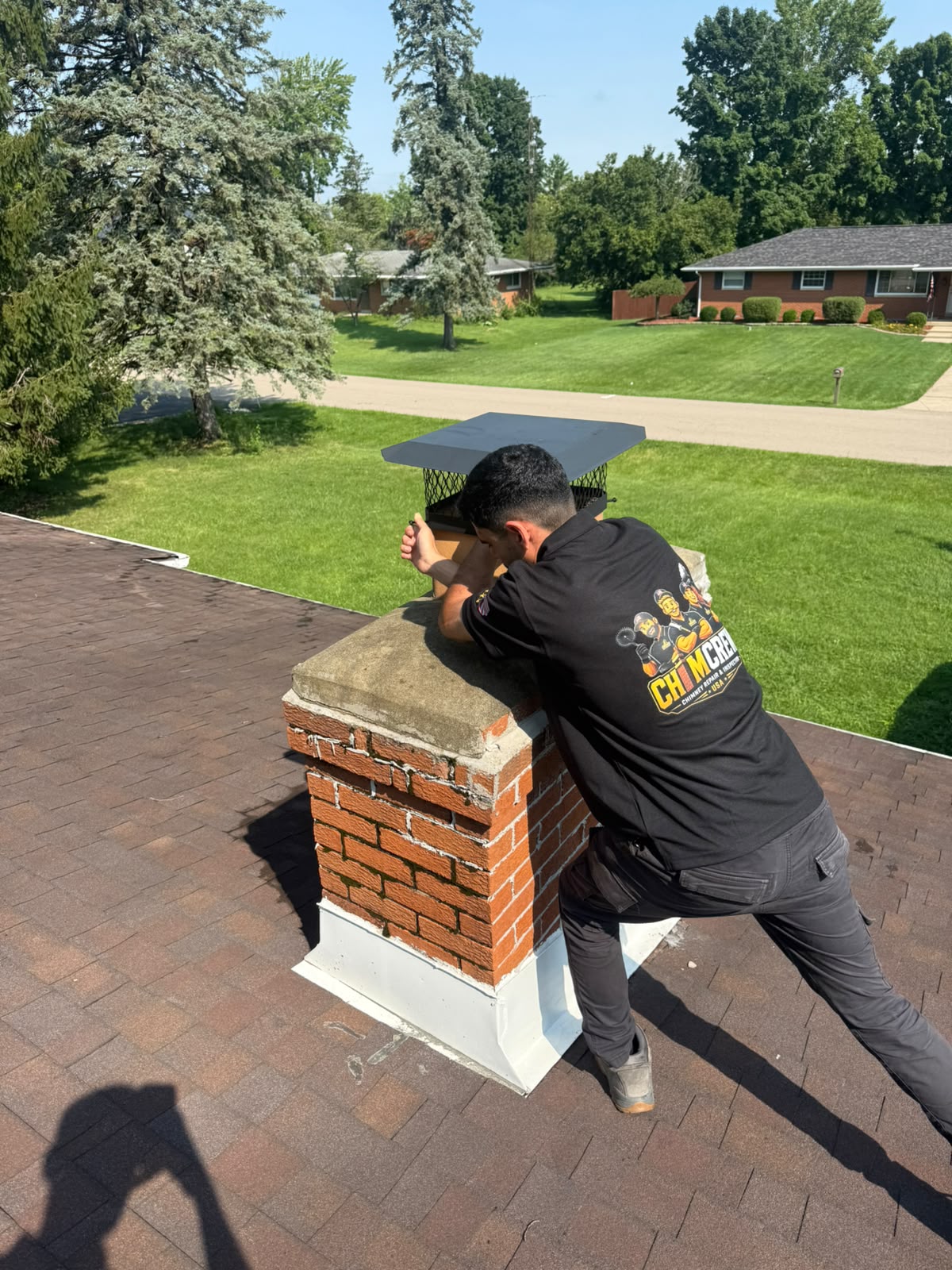 ChimCrew technician installing a stainless chimney cap on a brick chimney